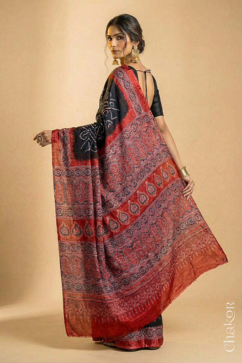 Woman wearing Black Bandhani Saree with Natural Red Ajrakh printed border and pallu in pure gaji silk with traditional bandhej tie-dye, handcrafted in Kutch.