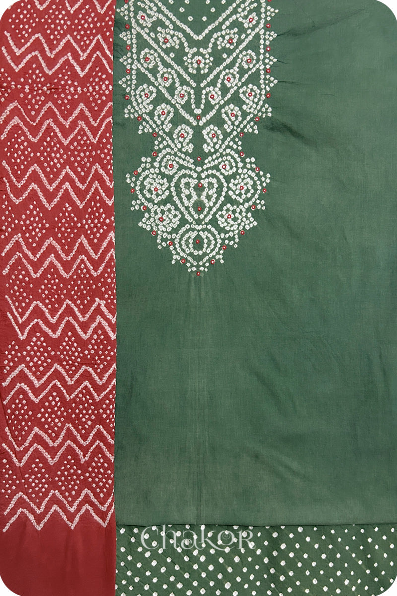 A moss green kurta set fabric with intricate bandhani & mirror embroidered yoke, paired with a matching bottom & brick red odhani placed on the left side featuring a zigzag design.