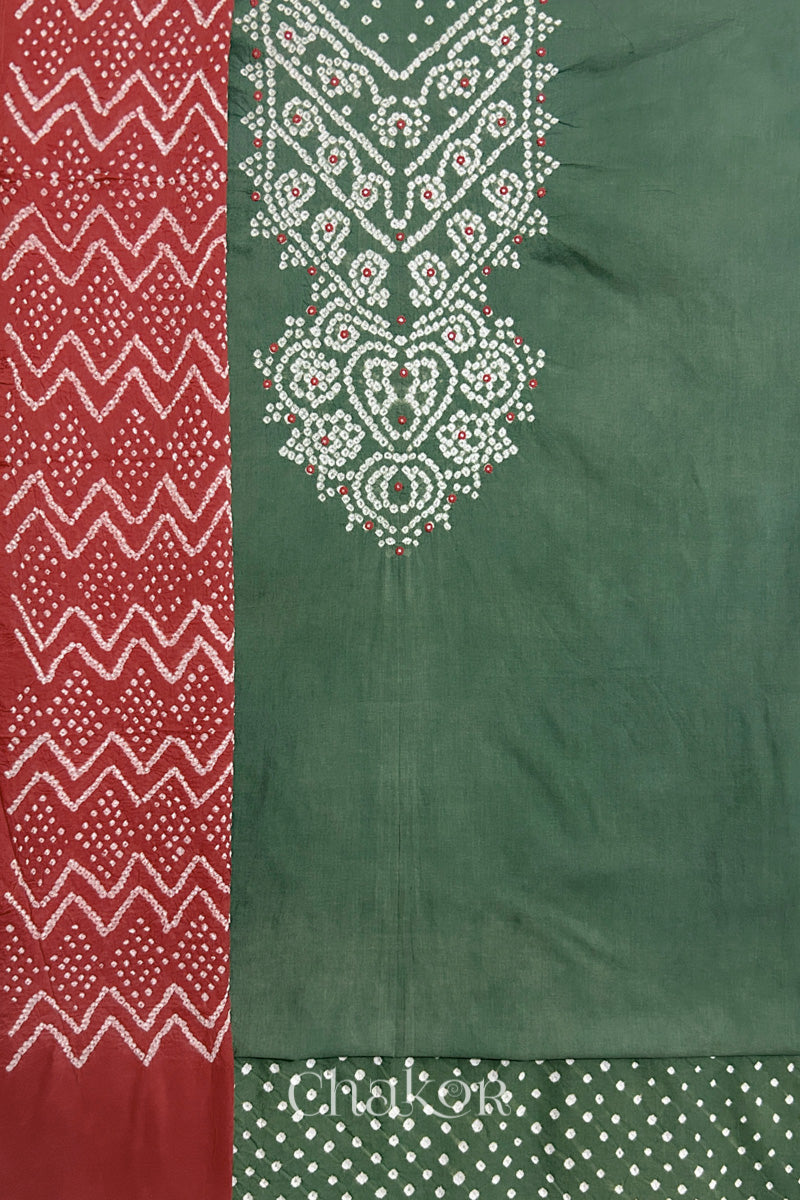 A moss green kurta set fabric with intricate bandhani & mirror embroidered yoke, paired with a matching bottom & brick red odhani placed on the left side featuring a zigzag design.