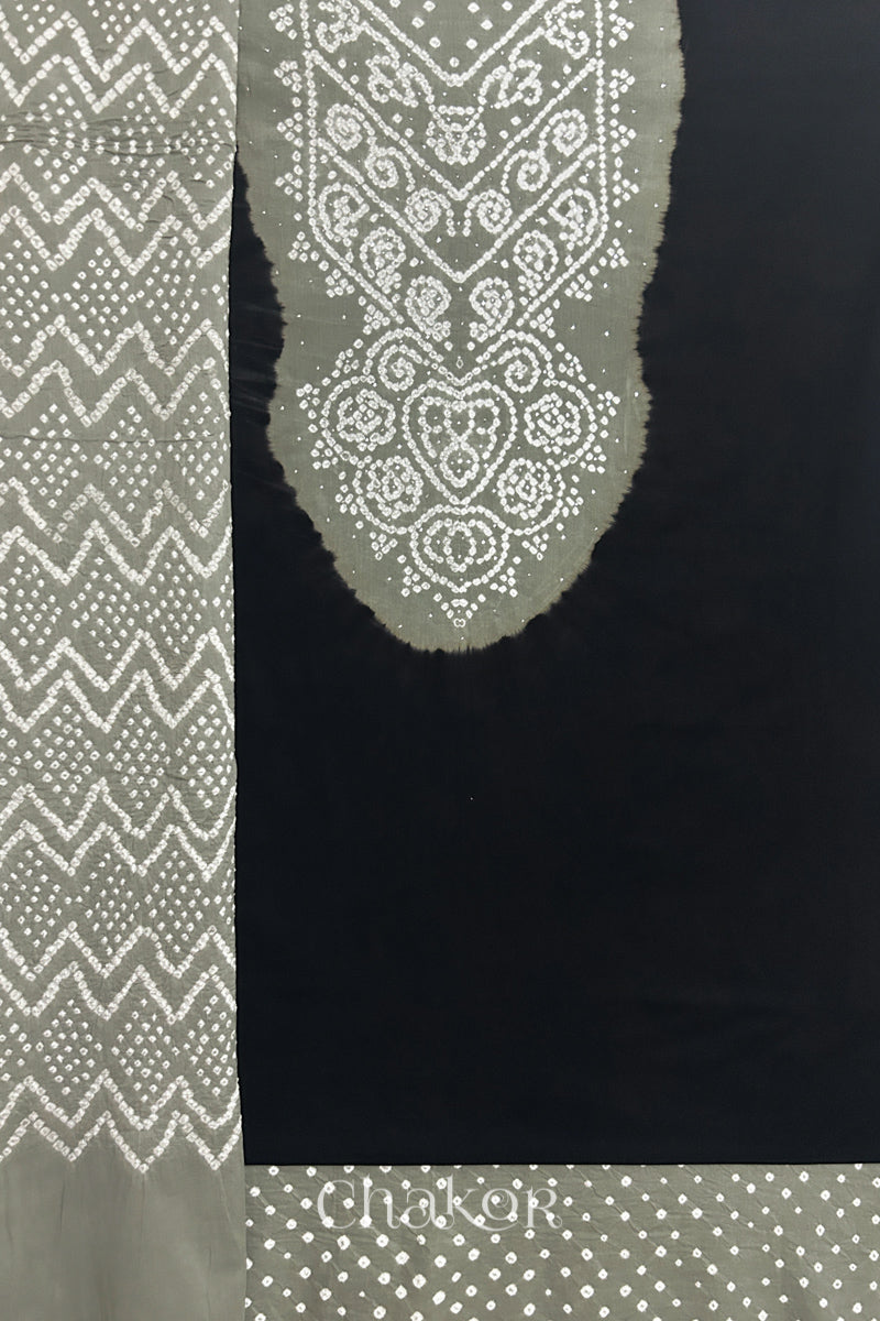 A black kurta set fabric with intricate bandhani & cement grey yoke with sparkly mukaish embroidery, paired with a bottom & odhani placed on the left side featuring a zigzag design.
