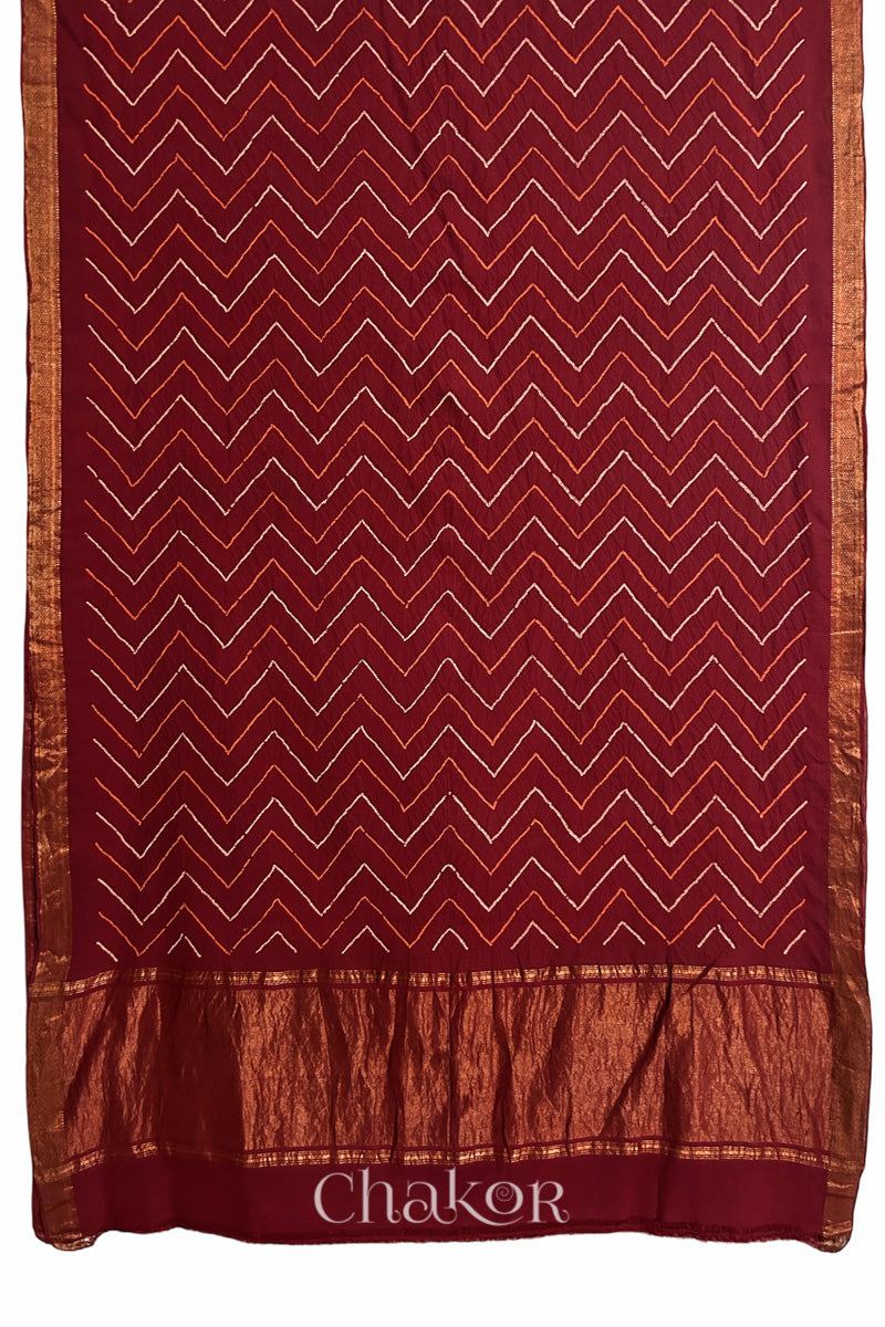Red saree, flat draped with Rai Bandhej zigzag pattern against white background and 'Chakor' brand watermark.