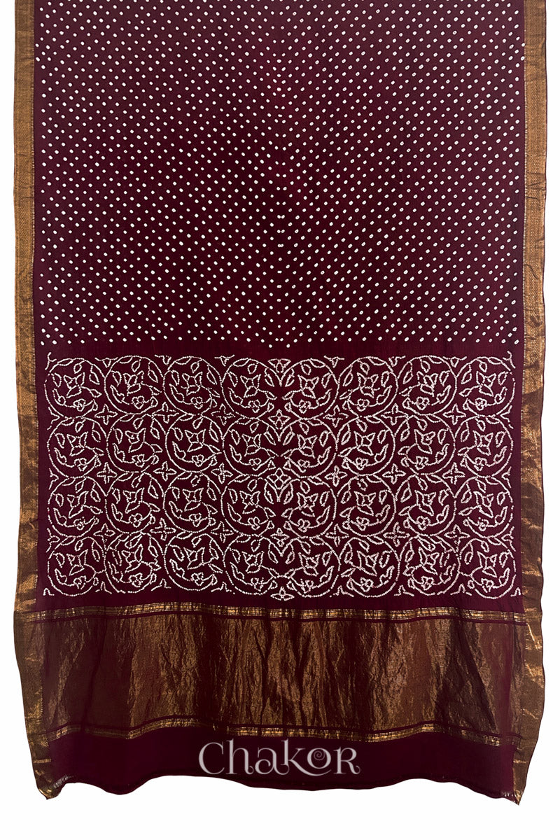 Maroon saree, flat draped with Rai Bandhej traditional design against white background and 'Chakor' watermark.