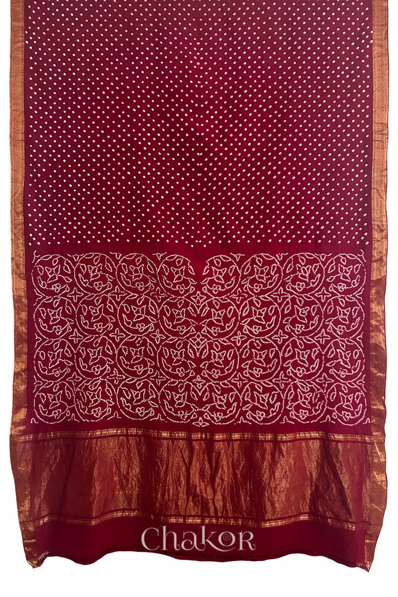 Red saree, flat draped with Rai Bandhej traditional design against white background and 'Chakor' watermark.