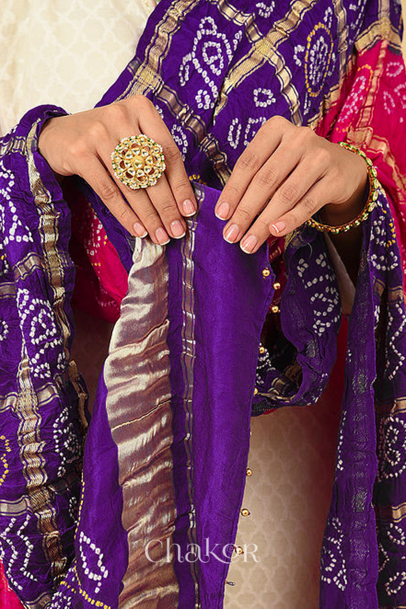 Close up of woman wearing Pink Purple Bandhani Gharchola Gaji Silk Dupatta on beige kurta set featuring zari check and beads edging on pallu.