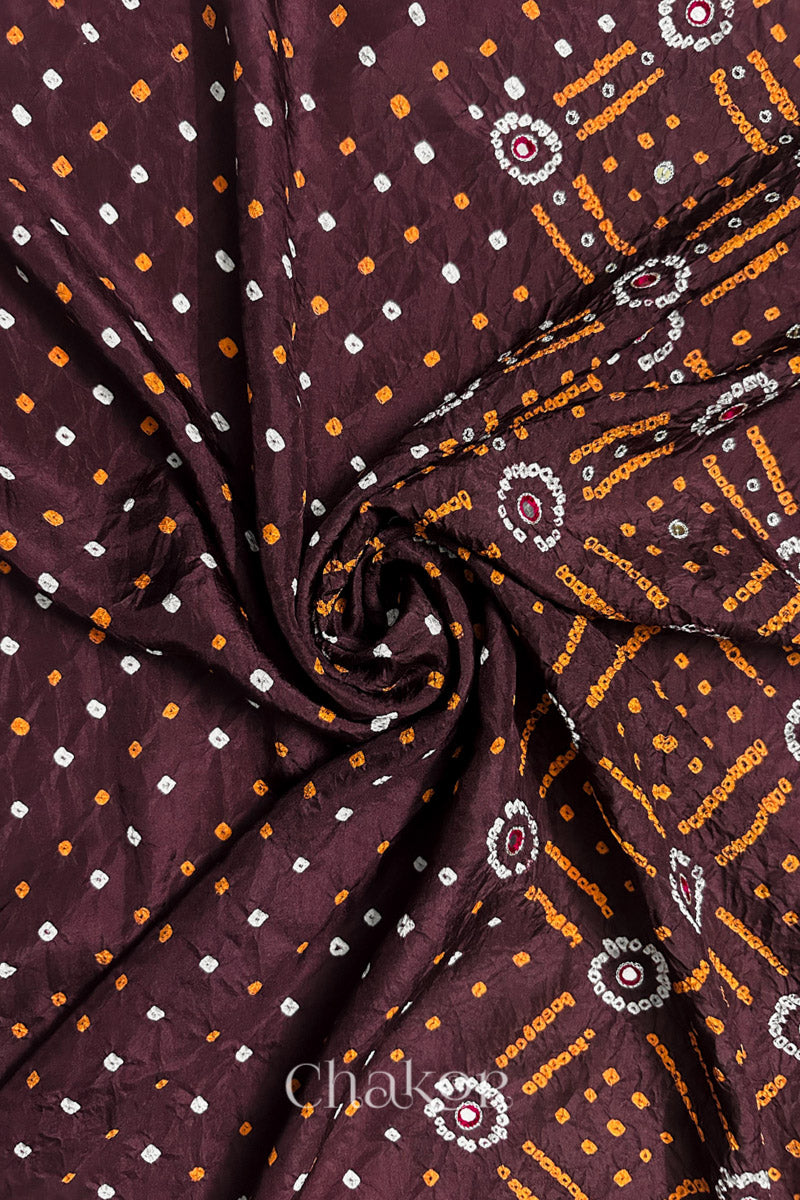 Maroon mulberry silk Bandhani (Rai Bandhej) fabric with white and yellow tie-dyed motifs, zari embroidered pink mirror & sequins embellishments, arranged in a swirling design  – CHAKOR.
