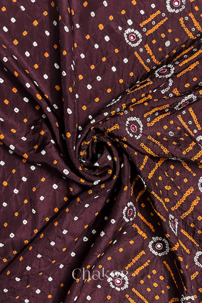 Maroon mulberry silk Bandhani (Rai Bandhej) fabric with white and yellow tie-dyed motifs, zari embroidered pink mirror & sequins embellishments, arranged in a swirling design  – CHAKOR.
