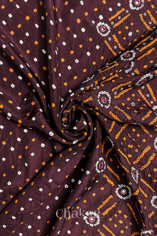 Maroon mulberry silk Bandhani (Rai Bandhej) fabric with white and yellow tie-dyed motifs, zari embroidered pink mirror & sequins embellishments, arranged in a swirling design  – CHAKOR.
