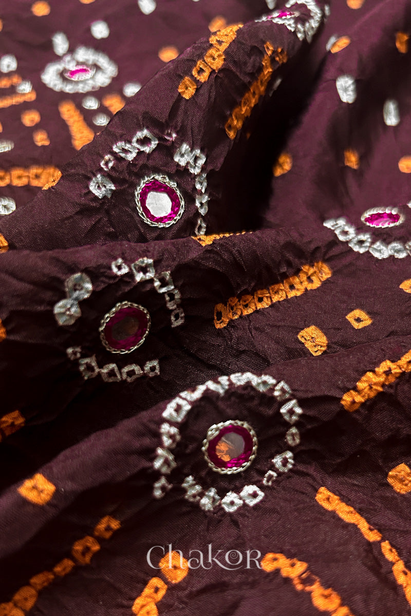 Close-up of Maroon mulberry silk Bandhani (Rai Bandhej) fabric with white and yellow  tie-dye motifs, zari embroidered pink mirror work and sequin detailing – CHAKOR.
