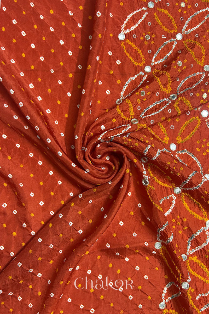 Rusty Orange mulberry silk Bandhani (Rai Bandhej) fabric with white tie-dyed motifs, golden zari mirror and sequin embellishment, arranged in a swirling design  – CHAKOR.
