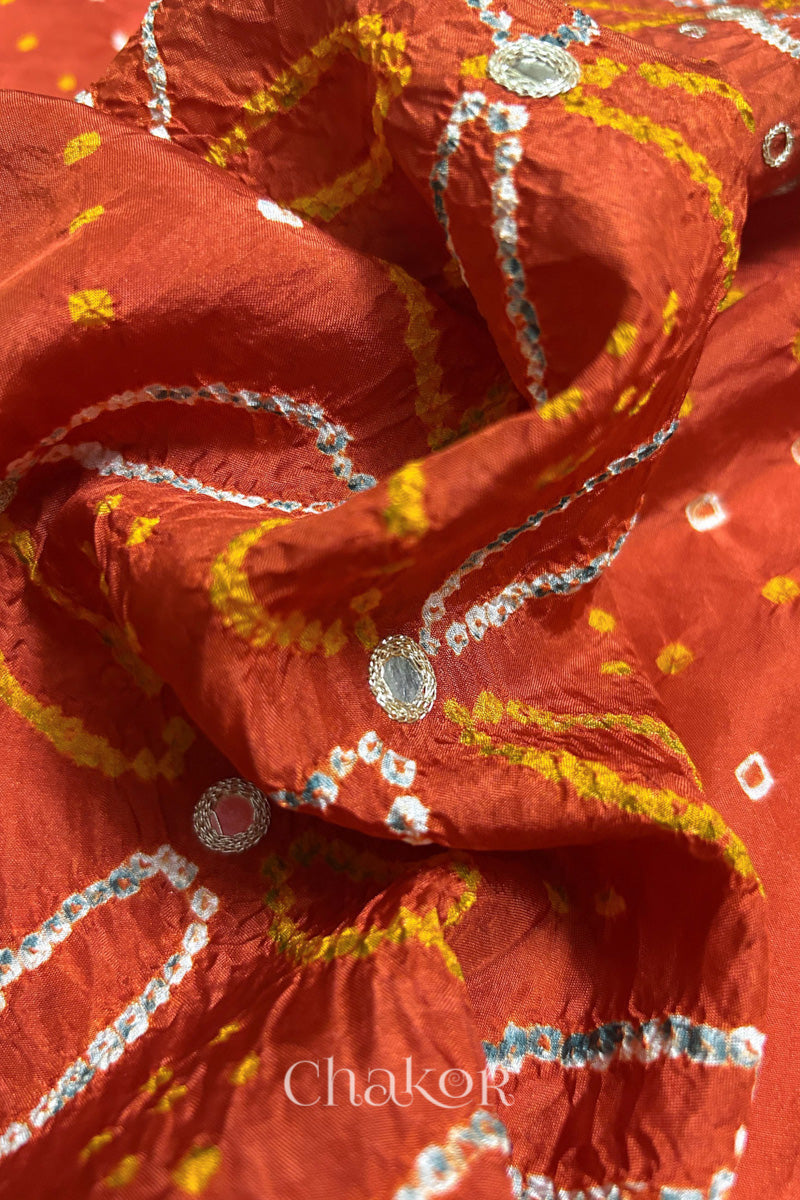 Close-up of Rusty Orange mulberry silk Bandhani (Rai Bandhej) fabric with white tie-dye motifs, golden zari embroidered golden zari mirror work and sequin detailing – CHAKOR.
