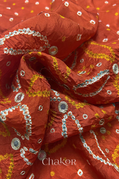 Close-up of Rusty Orange mulberry silk Bandhani (Rai Bandhej) fabric with white tie-dye motifs, golden zari embroidered golden zari mirror work and sequin detailing – CHAKOR.
