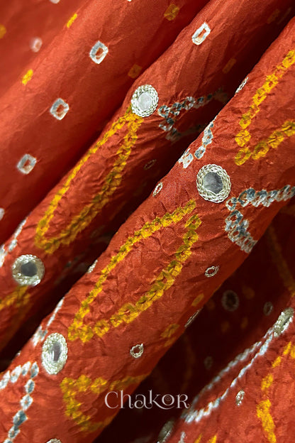Close-up of Rusty Orange mulberry silk Bandhani (Rai Bandhej) fabric with white tie-dye motifs, golden zari embroidered golden zari mirror work and sequin detailing – CHAKOR.
