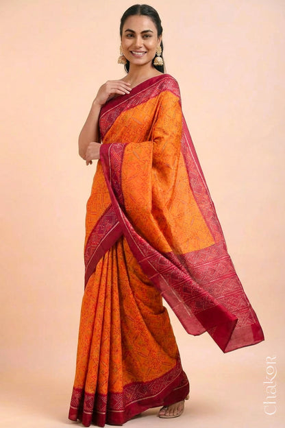 Model wearing Handloom Orange Rajkoti Patola Ikat Mulberry Silk Saree with red borders pallu, woven using traditional designs in Gujarat.