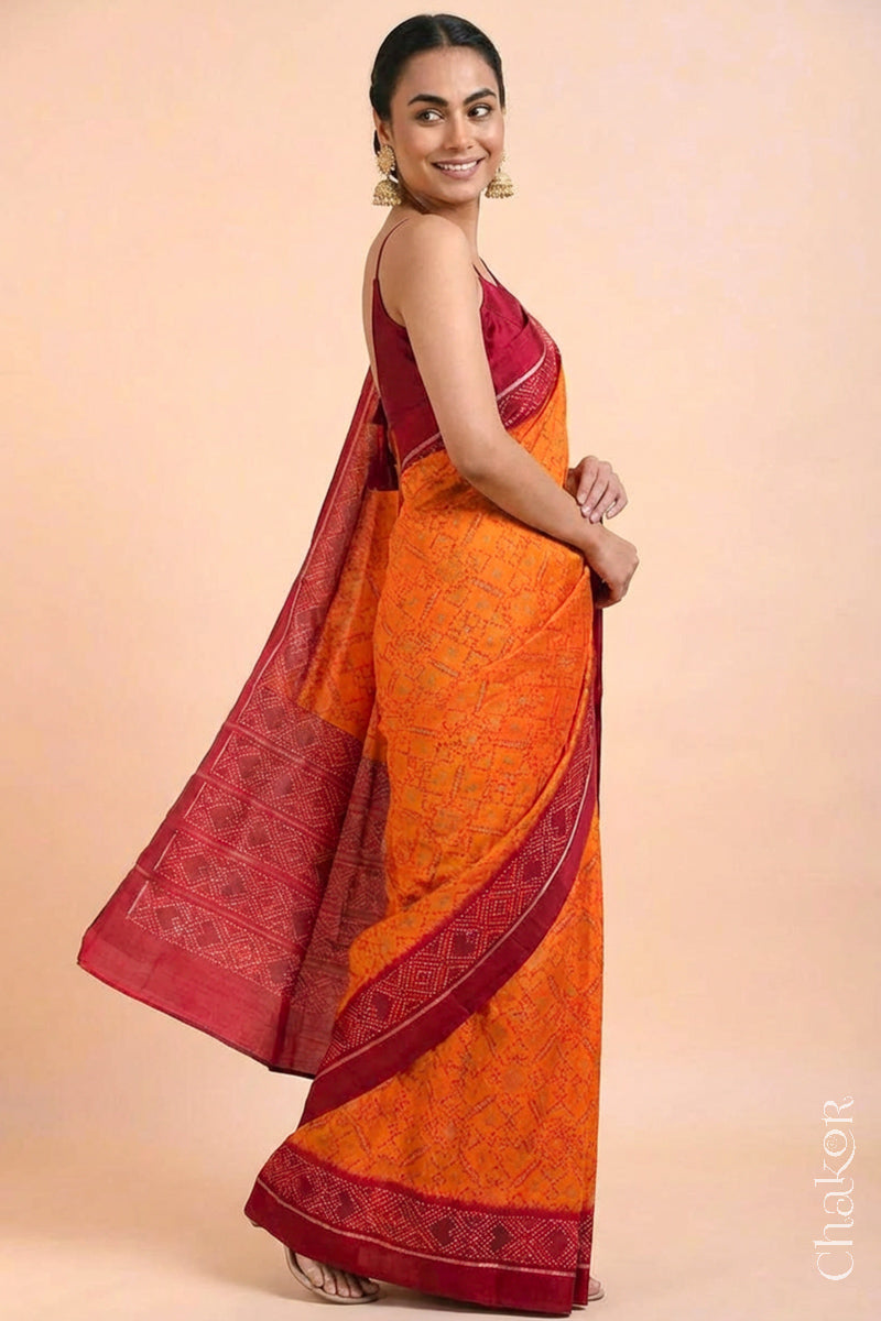 Model wearing Handloom Orange Rajkoti Patola Ikat Mulberry Silk Saree with red borders pallu, woven using traditional designs in Gujarat.