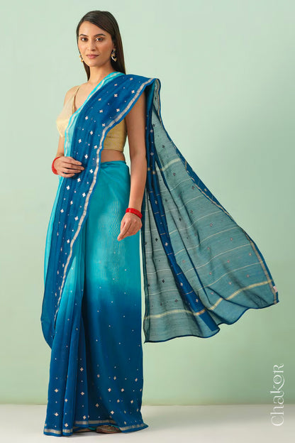Model wearing a turquoise navy shaded Chanderi silk cotton saree with hand-embroidered sequin and zari details.
