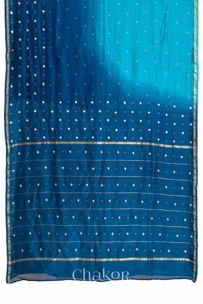 Flat view of turquoise navy shaded Chanderi silk cotton saree showing ombre transition and border finish.
