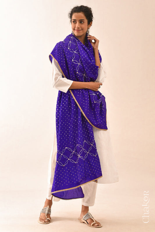 Women wearing purple Bandhani mulberry silk dupatta with tie-dye dot pattern & detailed with mirror work & golden lace on edge draped over a white kurta.