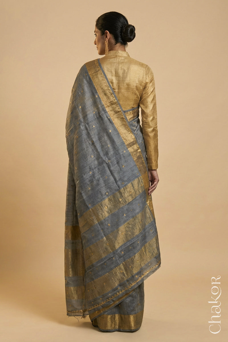 Back Pose of Woman wearing a Grey tussar silk handloom saree with golden zari border & hand embroidered with  sequins & zari work