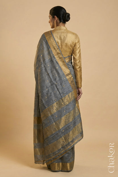 Back Pose of Woman wearing a Grey tussar silk handloom saree with golden zari border & hand embroidered with  sequins & zari work