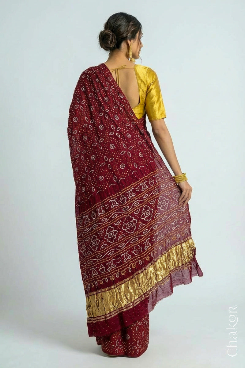 Back pose of Model wearing Handcrafted Maroon Bandhani Gaji Silk Saree with traditional rai bandhej patterns and mukaish embroidery.
