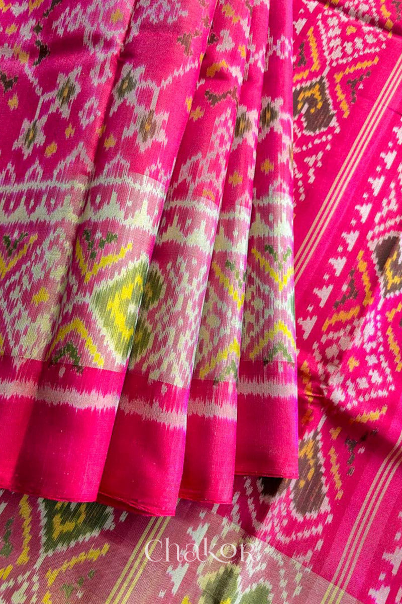 Close up of Handloom Rani Pink Rajkoti Patola Ikat Mulberry Silk Saree with tissue borders, and mauve pallu woven using traditional designs in Gujarat.