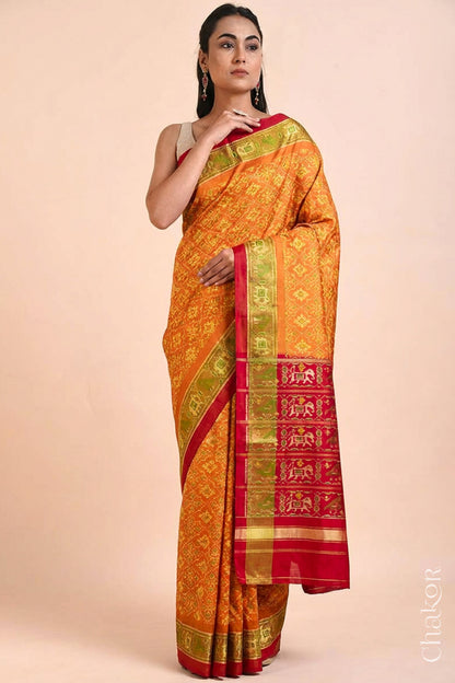 Model wearing Handloom Rust Rajkoti Patola Ikat Mulberry Silk Saree with Red borders & pallu, woven using traditional designs in Gujarat.