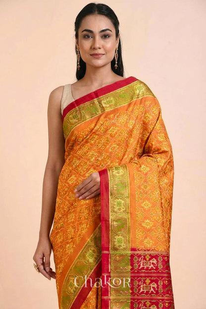Model wearing Handloom Rust Rajkoti Patola Ikat Mulberry Silk Saree with Red borders & pallu, woven using traditional designs in Gujarat.