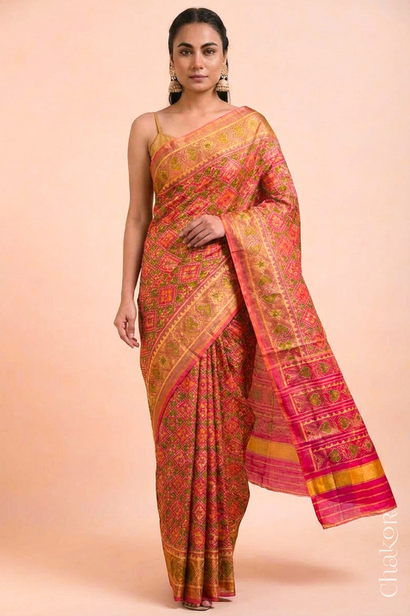 Model wearing Handloom Coral Peach Rajkoti Patola Ikat Mulberry Silk Saree with tissue borders, woven using traditional designs in Gujarat.