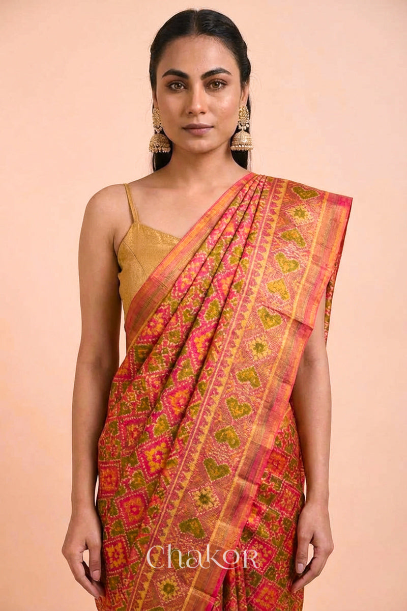 Model wearing Handloom Coral Peach Rajkoti Patola Ikat Mulberry Silk Saree with tissue borders, woven using traditional designs in Gujarat.