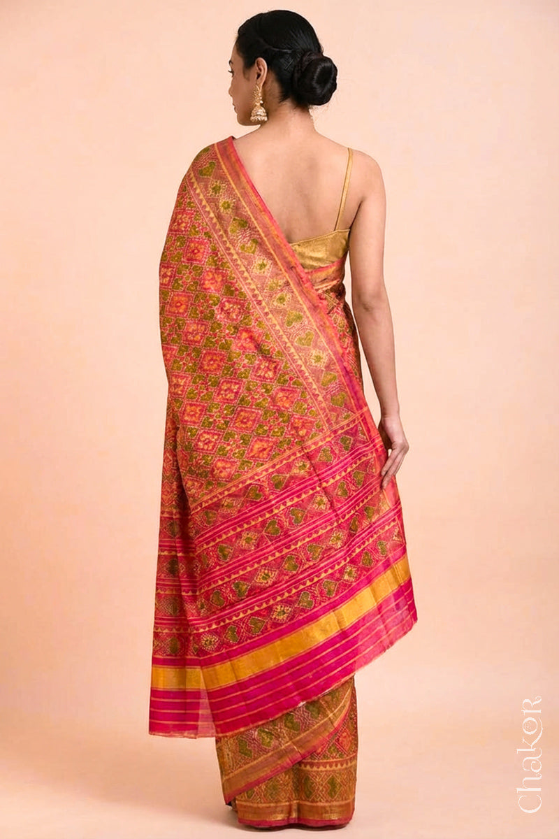 Model wearing Handloom Coral Peach Rajkoti Patola Ikat Mulberry Silk Saree with tissue borders, and pink pallu woven using traditional designs in Gujarat.
