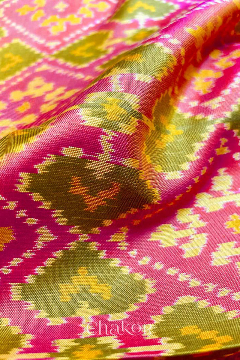 Close up of Handloom Coral Peach Rajkoti Patola Ikat Mulberry Silk Saree with tissue borders, and pink pallu woven using traditional designs in Gujarat.
