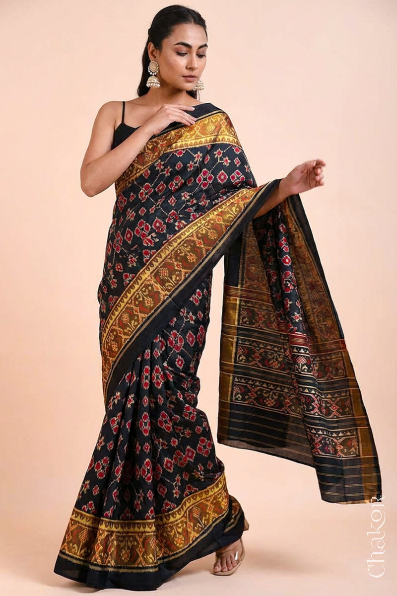 Model wearing Handloom Black Patola Ikkat Mulberry Silk Saree with traditional patterns in red floral motifs.