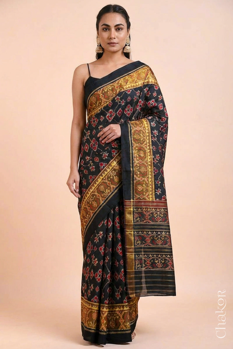 Model wearing Handloom Black Patola Ikkat Mulberry Silk Saree with traditional patterns in red floral motifs.
