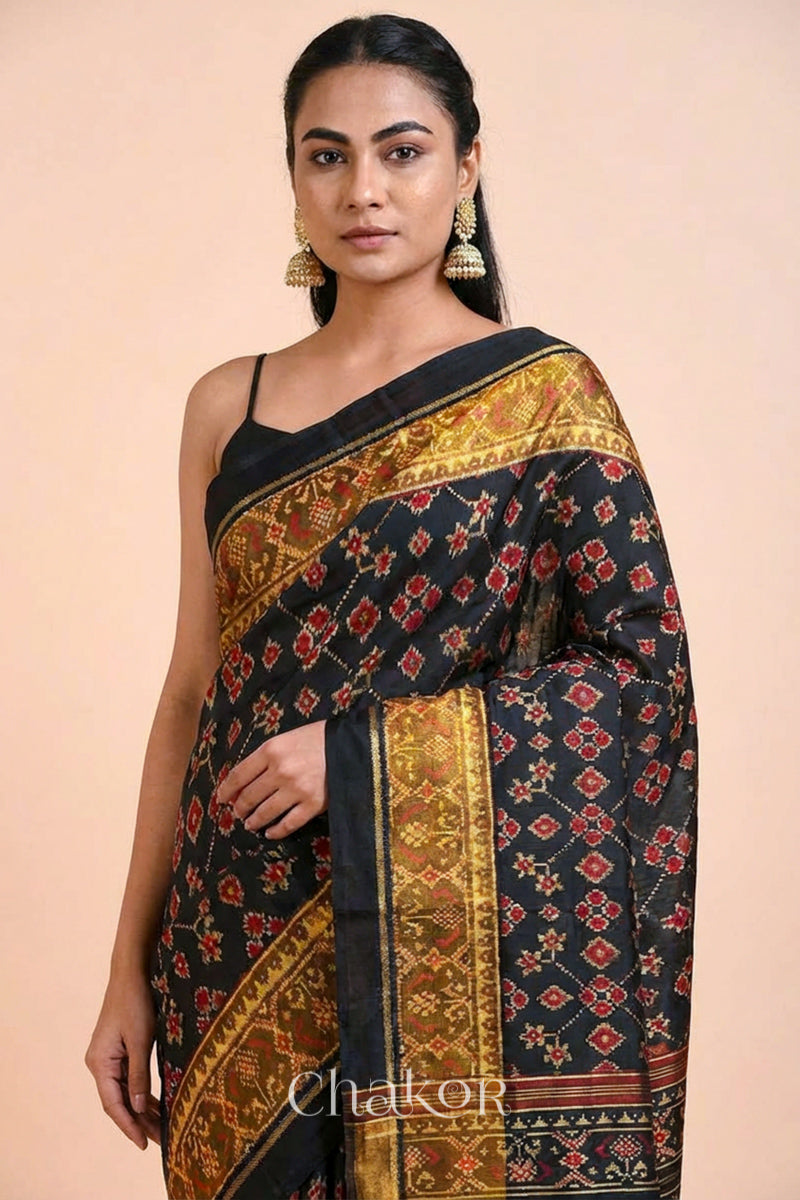 Model wearing Handloom Black Patola Ikkat Mulberry Silk Saree with traditional patterns in red floral motifs.
