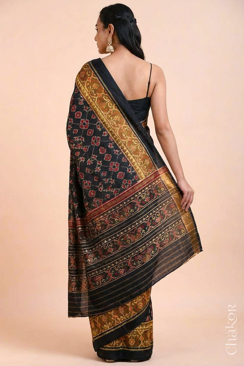 Model wearing Handloom Black Patola Ikkat Mulberry Silk Saree with traditional patterns in red floral motifs.