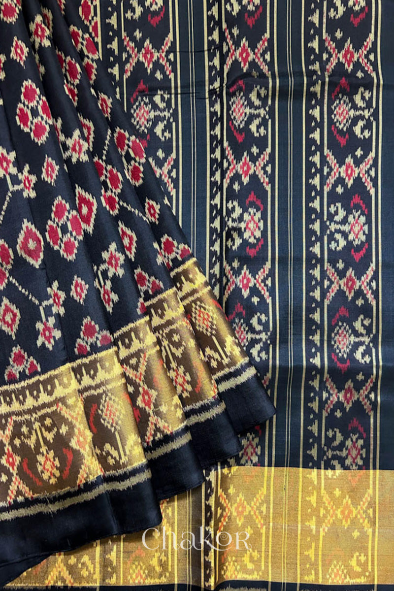Pleats laid flat on pallu view of Handloom Black Patola Ikkat Mulberry Silk Saree with traditional patterns in red floral motifs.