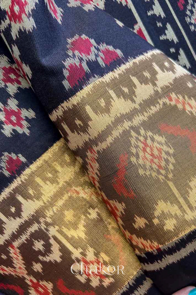 Close up of Handloom Black Patola Ikkat Mulberry Silk Saree with traditional patterns in red floral motifs featuring tissue ikat border.