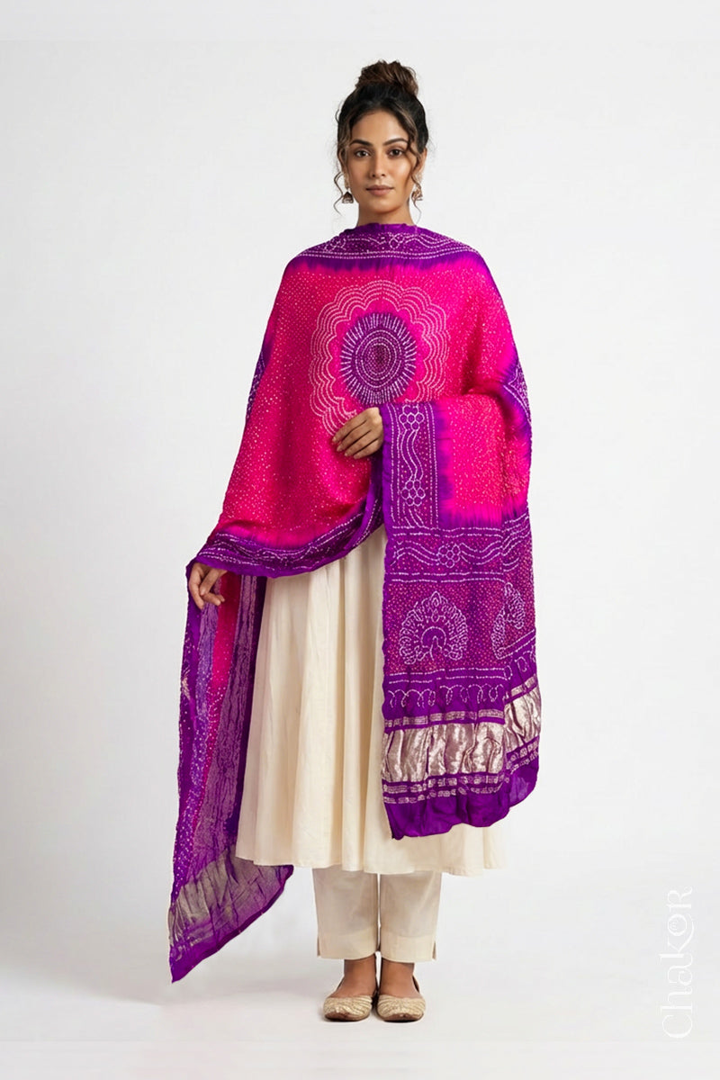 Model wearing pink and purple Bandhani gaji silk dupatta with peacock design pallu and contrast border.