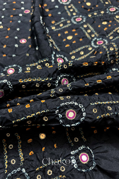 Close-up of Black mulberry silk Bandhani (Rai Bandhej) fabric with white and yellow tie-dye motifs, zari embroidered pink mirror work and sequin detailing – CHAKOR.
