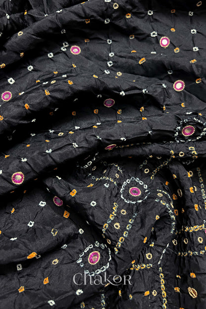 Close-up of Black mulberry silk Bandhani (Rai Bandhej) fabric with white and yellow tie-dye motifs, zari embroidered pink mirror work and sequin detailing – CHAKOR.
