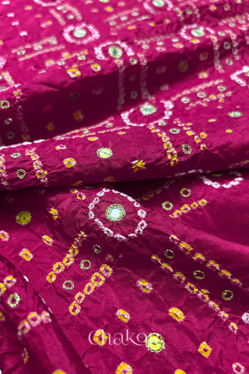 Close-up of Rani Pink mulberry silk Bandhani (Rai Bandhej) fabric with white and yellow tie-dye motifs, golden zari embroidered mirror work and sequin detailing – CHAKOR.
