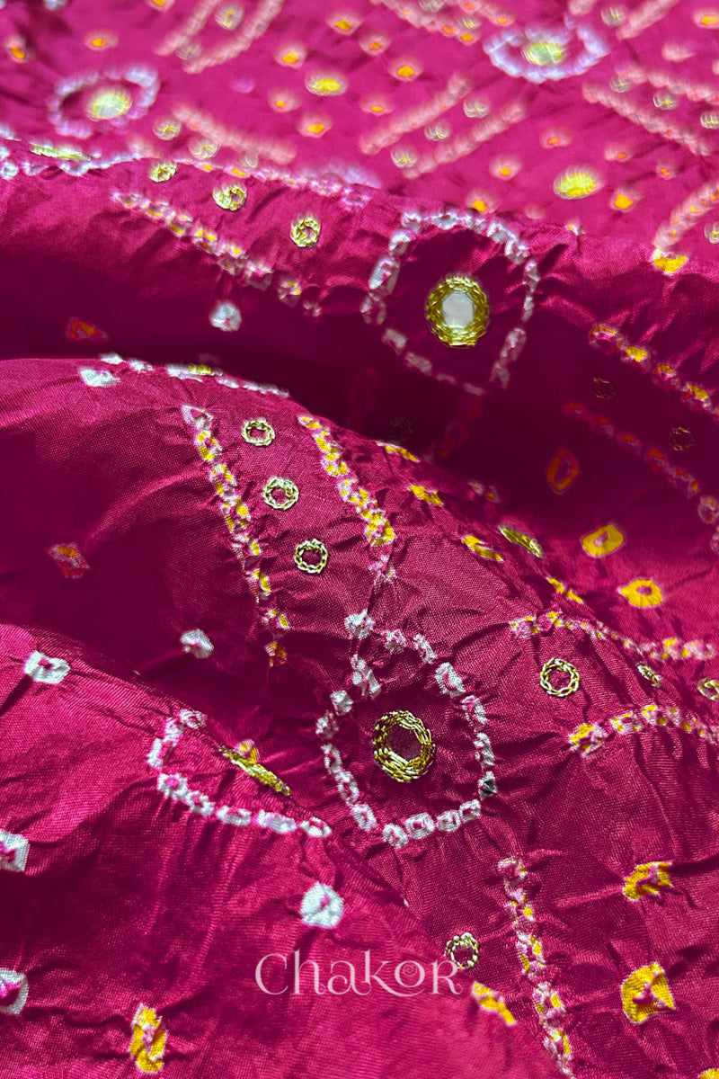 Close-up of Rani Pink mulberry silk Bandhani (Rai Bandhej) fabric with white and yellow tie-dye motifs, golden zari embroidered mirror work and sequin detailing – CHAKOR.
