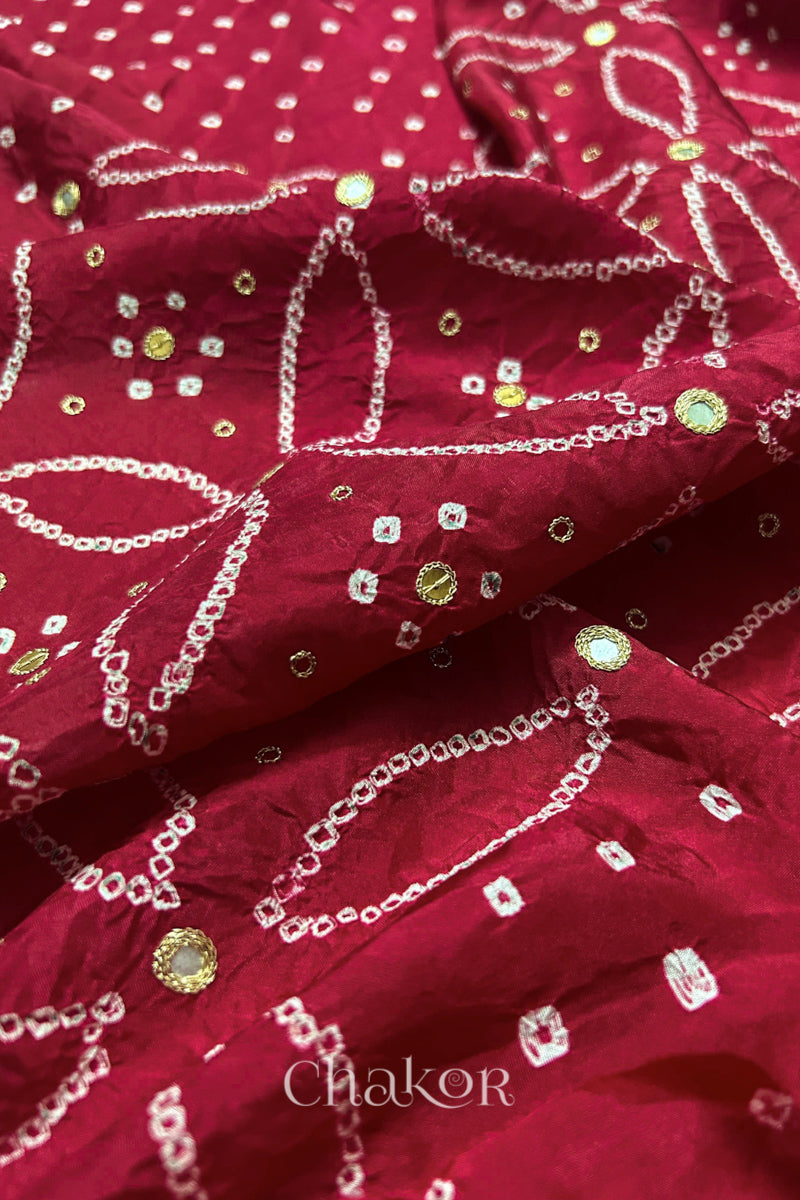 Close-up of Deep Red mulberry silk Bandhani (Rai Bandhej) fabric with white tie-dye motifs, golden zari embroidered mirror work and sequin detailing – CHAKOR.
