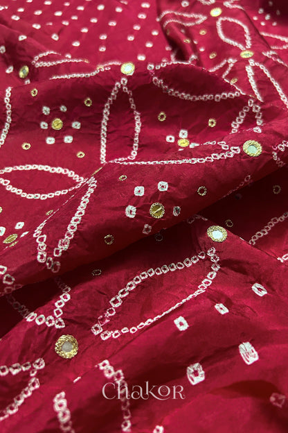 Close-up of Deep Red mulberry silk Bandhani (Rai Bandhej) fabric with white tie-dye motifs, golden zari embroidered mirror work and sequin detailing – CHAKOR.
