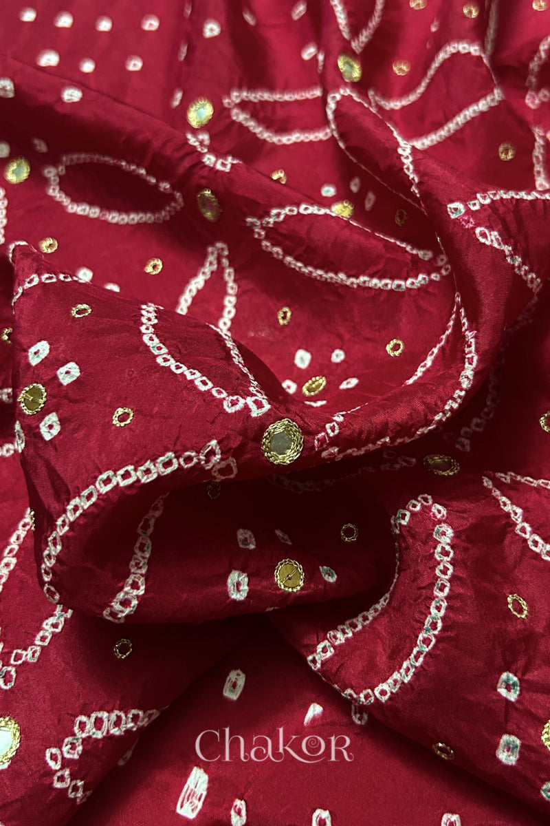 Close-up of Deep Red mulberry silk Bandhani (Rai Bandhej) fabric with white tie-dye motifs, golden zari embroidered mirror work and sequin detailing – CHAKOR.
