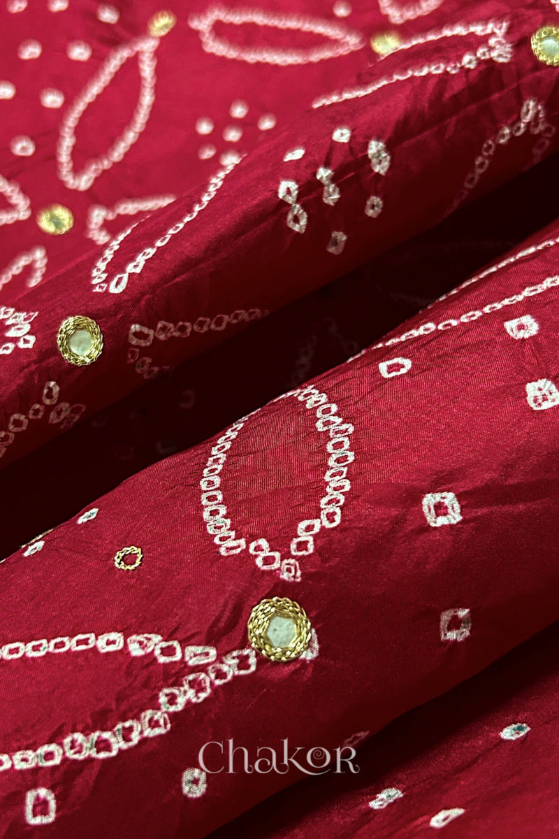 Close-up of Deep Red mulberry silk Bandhani (Rai Bandhej) fabric with white tie-dye motifs, golden zari embroidered mirror work and sequin detailing – CHAKOR.
