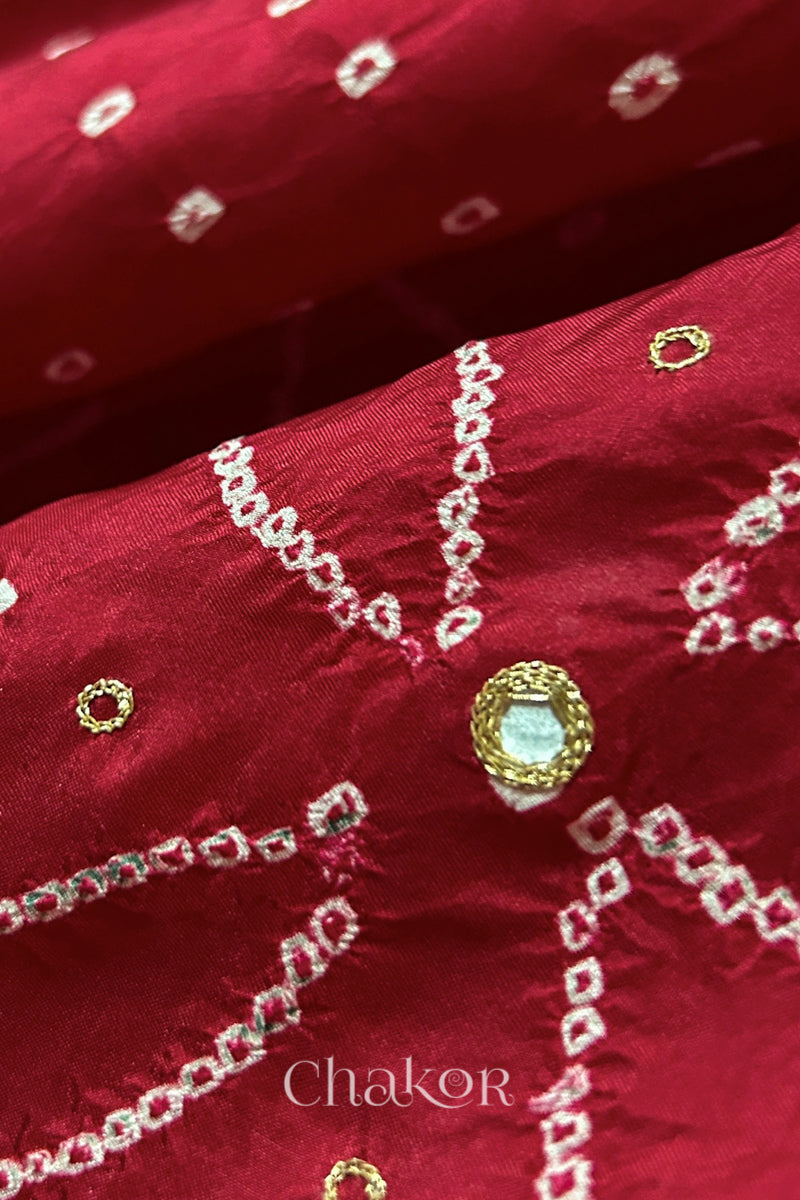 Close-up of Deep Red mulberry silk Bandhani (Rai Bandhej) fabric with white tie-dye motifs, golden zari embroidered mirror work and sequin detailing – CHAKOR.
