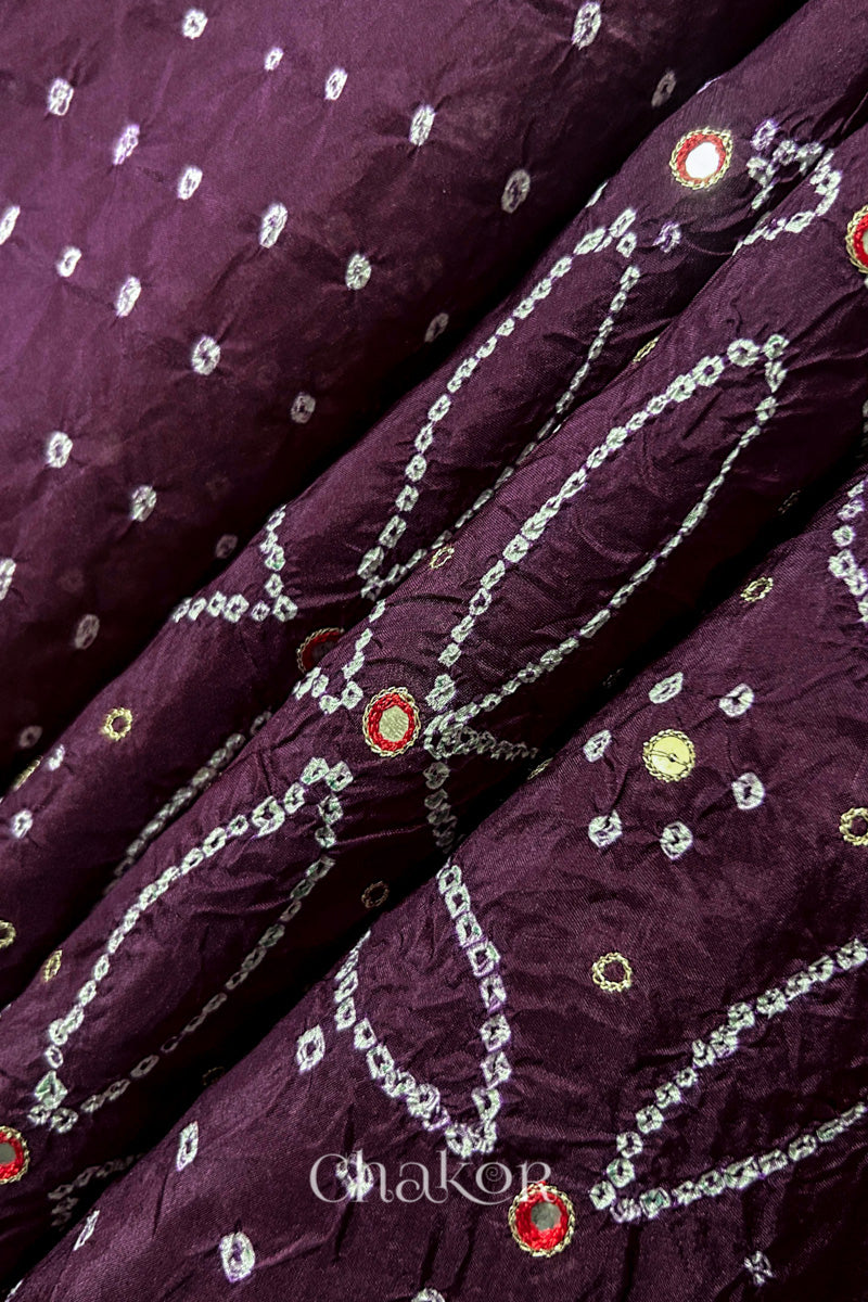 Close-up of Maroon mulberry silk Bandhani (Rai Bandhej) fabric with white tie-dye motifs, zari embroidered red mirror work and sequin detailing – CHAKOR.

