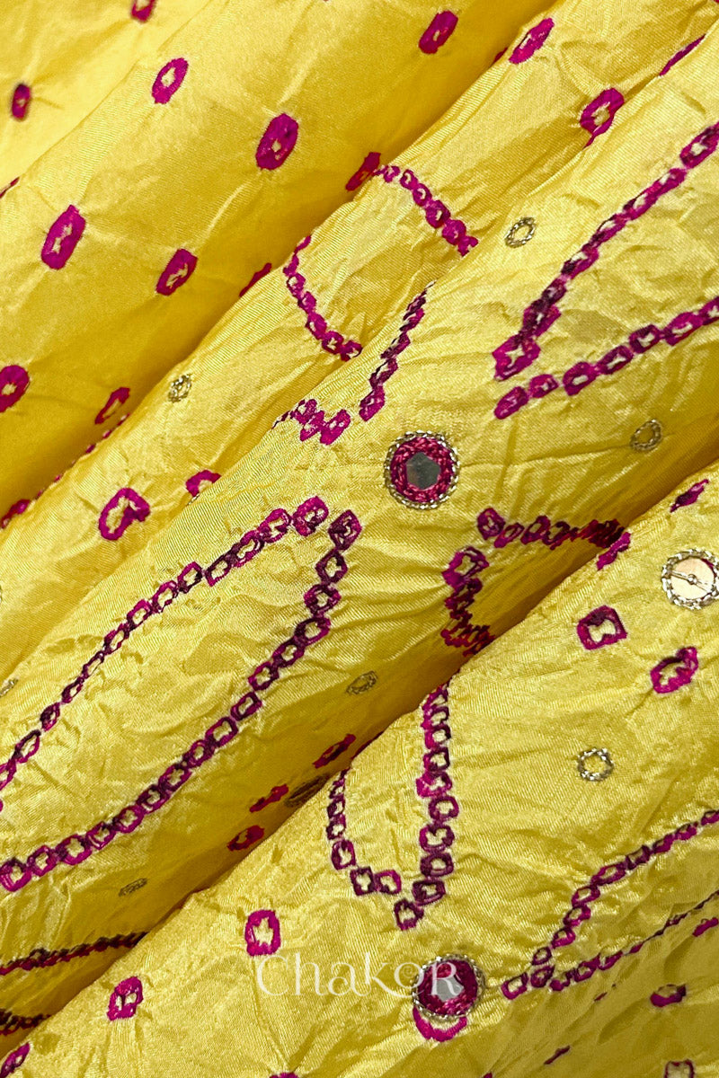 Close-up of Yellow mulberry silk Bandhani (Rai Bandhej) fabric with rani pink tie-dye motifs, zari embroidered pink mirror work and sequin detailing – CHAKOR.
