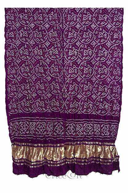 A vibrant magenta dupatta showcasing intricate rai bandhej in red & yellow with a shimmering gold band on the pallu and beads on the hem. Text reads Chakor brand watermark.
